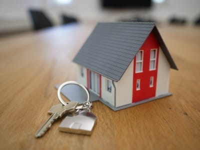 A miniature house sitting on a table with a set of keys placed beside it